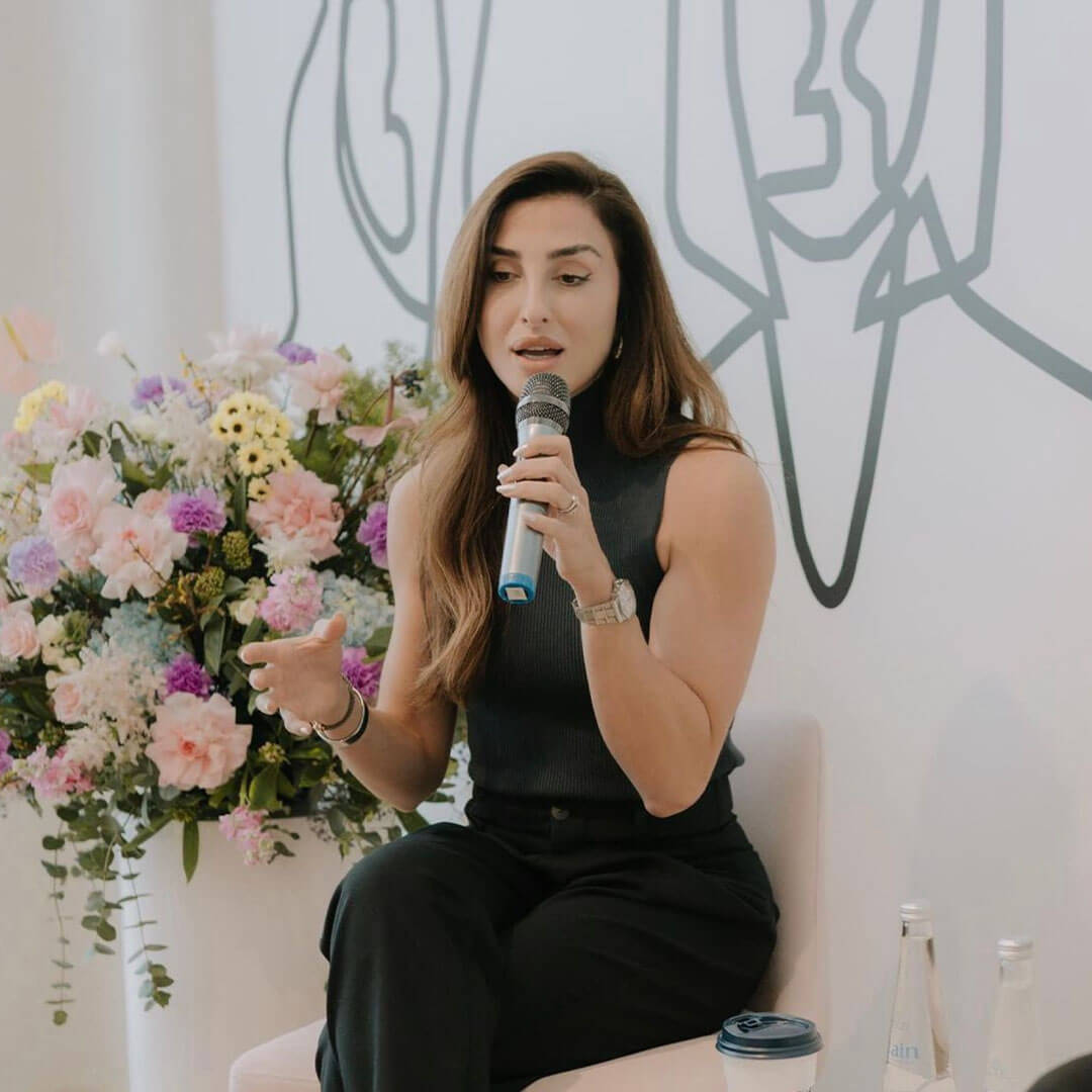 beautiful lady in black dress hosting an event againts a backdrop of pink flowers